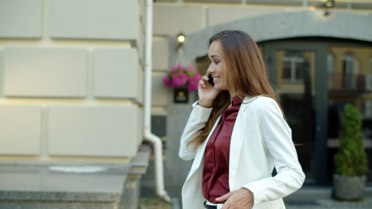 사업가 여성이 밖에서 전화를 하고 있습니다. 여성은 밖에서 스마트폰으로  ⁇ 고 있습니다.