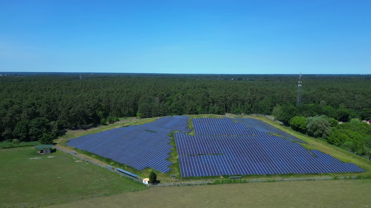 Photovoltaic panels providing clean energy in a solar farm on hill near a forest in Germany. Fantastic aerial view flight descending drone