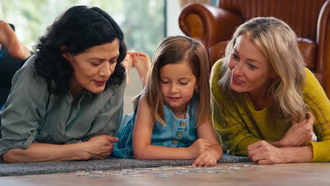 same sex family with two mature mums and daughter lying on floor doing jigsaw puzzle at home