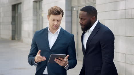 businessmen using digital tablet on city. male entrepreneurs talking outdoors
