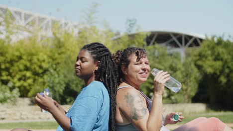 mujeres gordas cansadas sentadas de espaldas en el césped después del entrenamiento