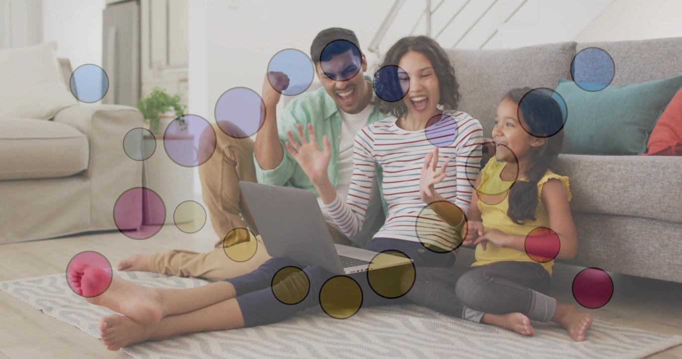 Mother opening laptop, family reacting and waving at screen, colorful circles obscuring faces, tech