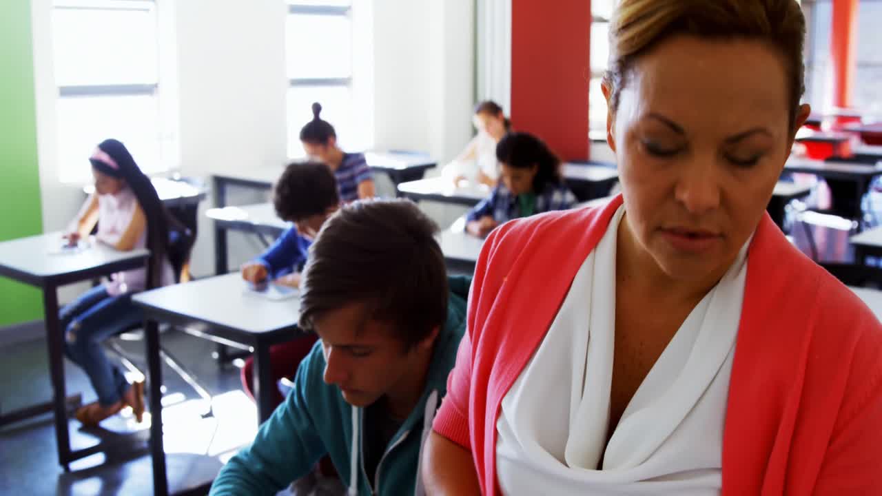 Teacher reading book while students using digital tablets in classroom