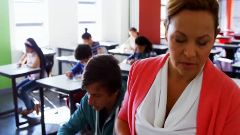 teacher reading book while students using digital tablets in classroom