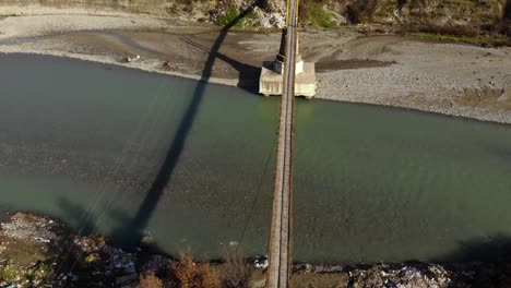 Puente-Colgante-Sobre-El-Río-Con-Agua-Fluyendo-En-Un-Día-Soleado,-Vista-Aérea