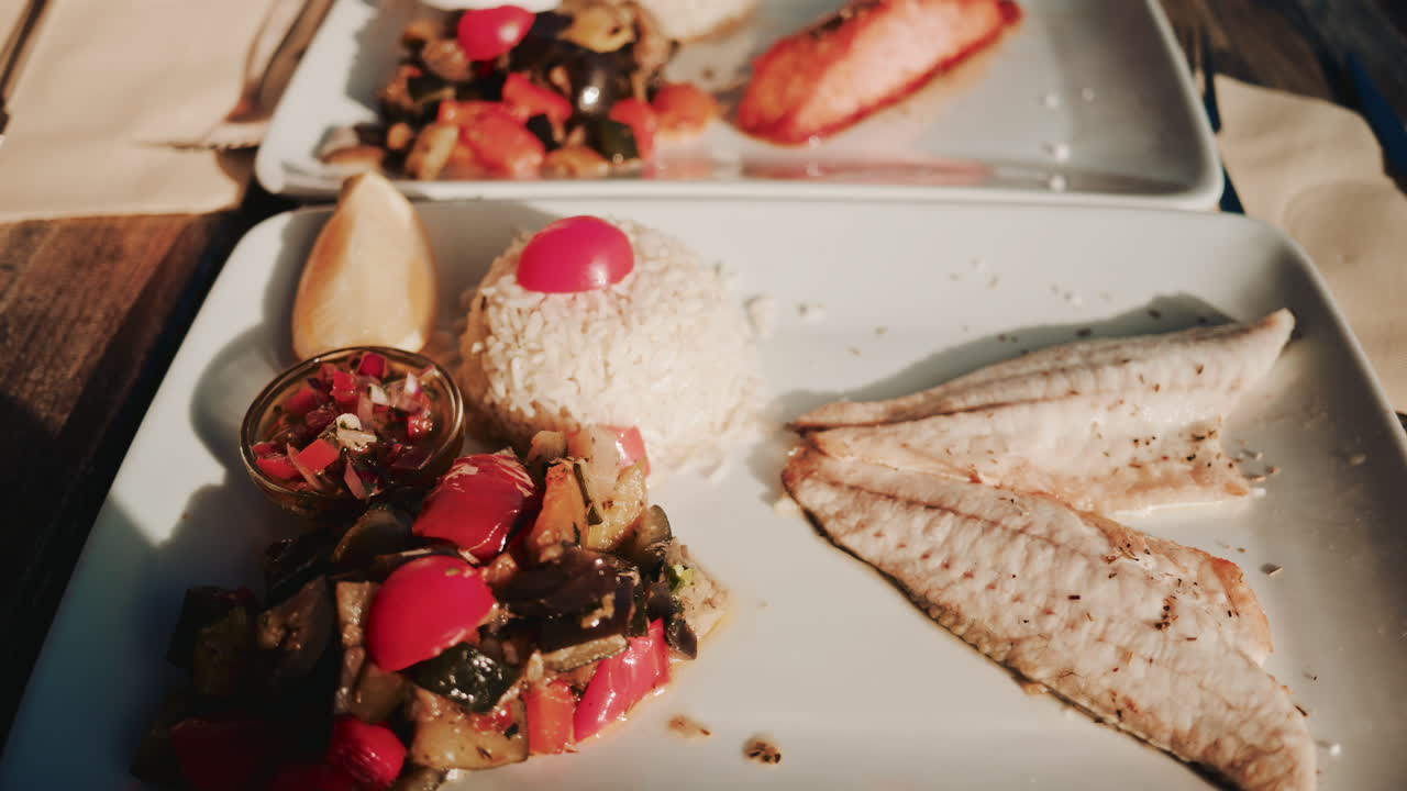 Two beautifully prepared seafood dishes are served on a wooden restaurant table in warm natural sunlight