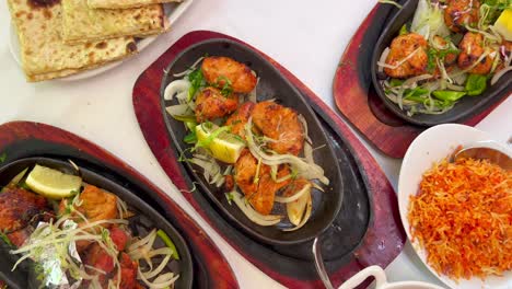 traditional indian tandoori chicken with onions on a very hot plate with steam smoke, butter chicken, cheese naan bread and coconut rice in a restaurant, authentic asian food, 4k top shot