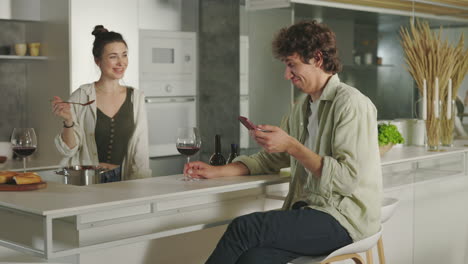 couple enjoys cooking and wine in a modern kitchen, with one partner feeding the other