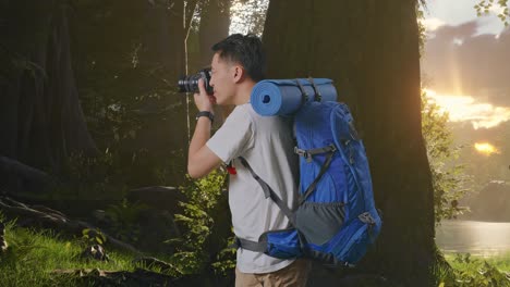 vista lateral de un excursionista masculino asiático con una mochila de montañismo usando una cámara tomando fotos mientras explora la naturaleza forestal