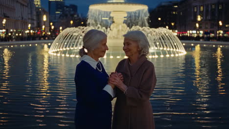 two elderly women holding hands by an illuminated fountain at night
