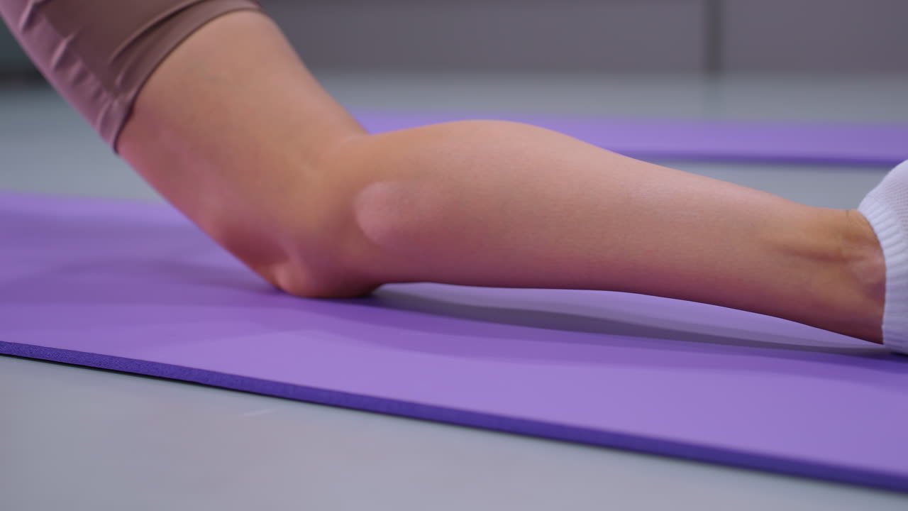 primer plano de estiramiento de piernas realizado en una alfombra de yoga púrpura, mostrando pierna y pie en calcetines blancos, enfatizando el detalle y la tensión durante una sesión de entrenamiento