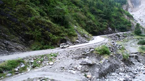 aerial of 4x4 safari jeep transporting tourists off-road up a green rocky mountain landscape in mustang nepal