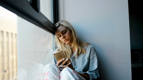 mujer preocupada usando teléfono móvil cerca de la ventana 4k