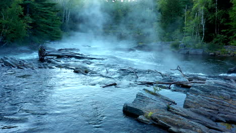 aerial drone shot sliding right across the dark misty forest stream at big wilson falls with logs and wet grey rocks in the waterfall at dusk in maine