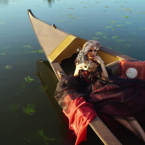 woman dressed in traditional costume with carnival mask lying in a boat in venice. attractive young sensual romantic woman floating in gondola in the evening.