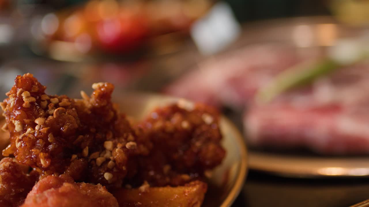 Camera glides over raw beef and fried chicken under warm, softly blurred restaurant lighting
