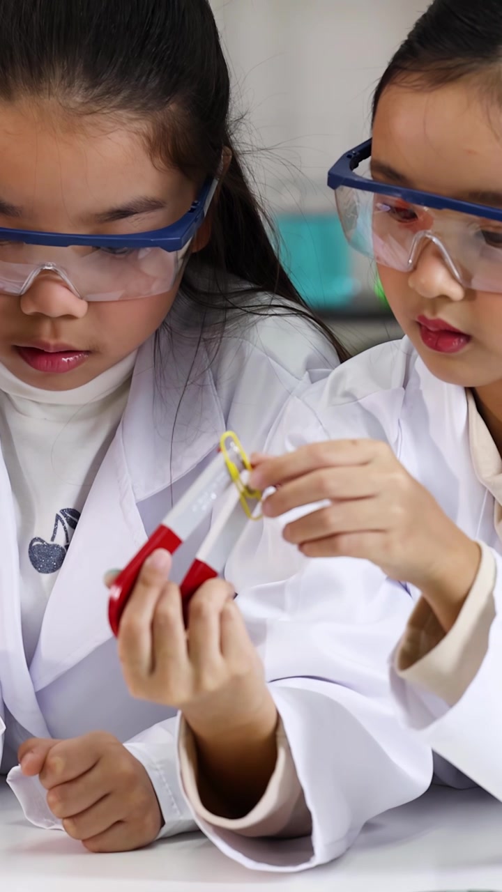 Siswa sekolah dasar mengenakan kacamata pengaman saat menguji daya tarik magnet di laboratorium kelas yang terang