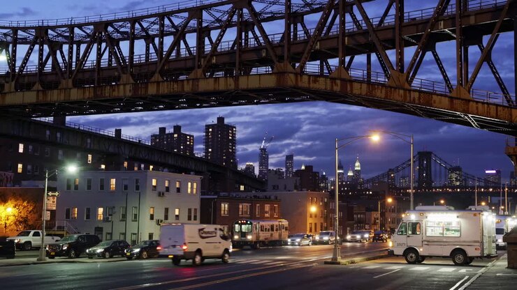 Urban evening scene video with a low-angle view of a busy street under a bridge, capturing city