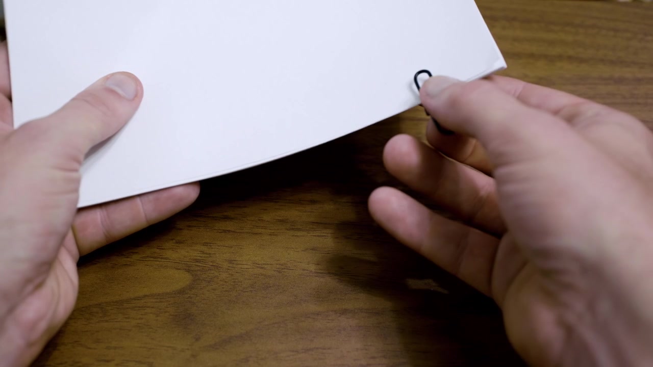 Primo piano di una mano che usa una graffetta per collegare una pila di fogli. Fogli A4 per stampante uniti con un fermacampioni
