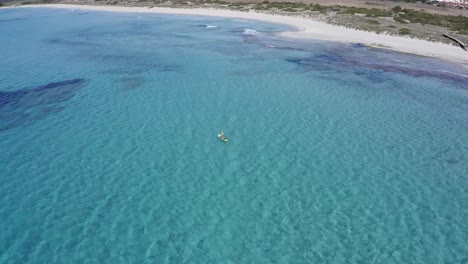 Paddle-boarder-going-along-the-coast-of-Son-Bou-beach,-Menorca