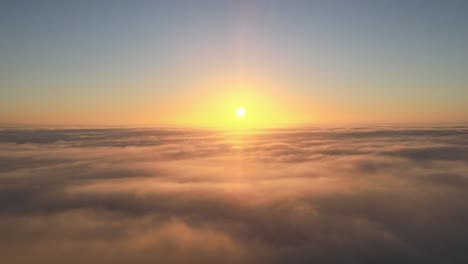 beautiful cinematic shot flying above clouds looking at the sun setting or rising on the horizon as the clouds move and eventually cover the sun