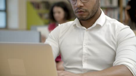 Front-view-of-focused-young-man-using-laptop-at-library