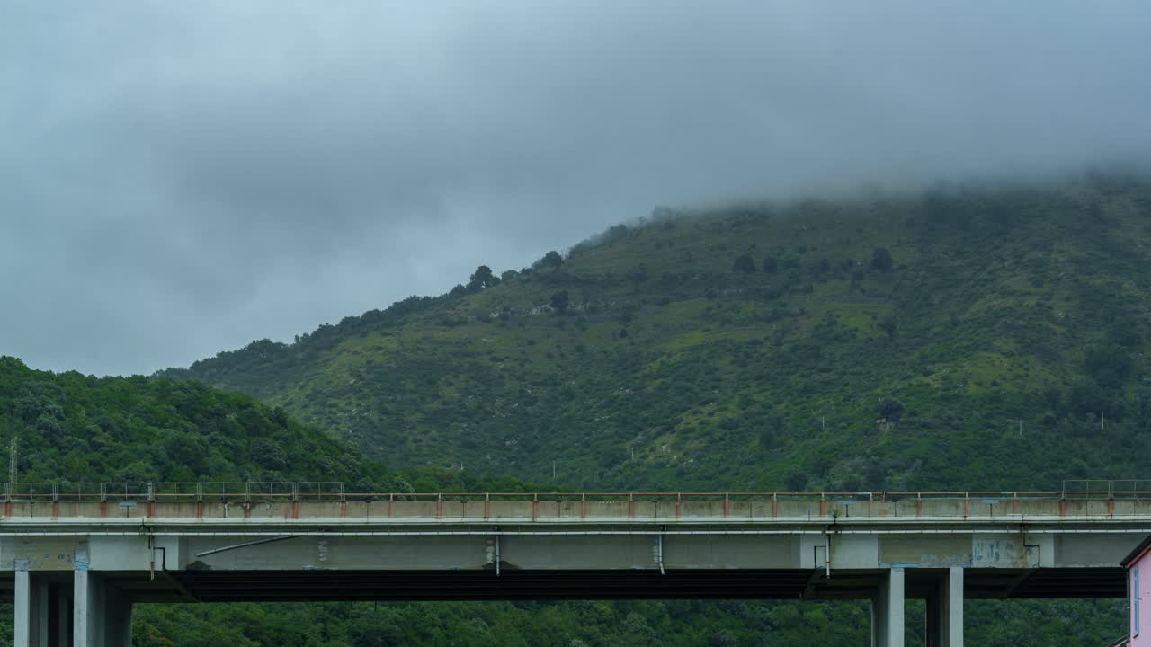 Traffic timelapse on bridge with clouds rolling over green hills in Genoa, Liguria, Italy