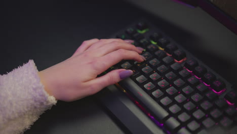 Hand view of lady with polished nails actively gaming on RGB backlit keyboard, soft ambient light reflecting on wrist, partial computer screen visible in background