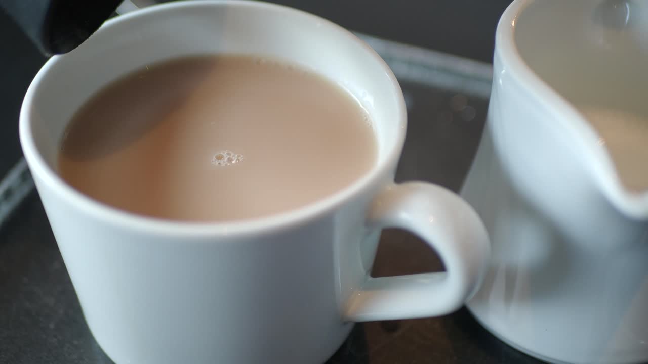 Close-up of a cup of coffee or tea with milk, next to a creamer