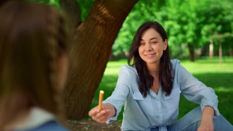 Mother-giving-bread-stick-to-daughter-close-up.-Family-lunching-on-picnic