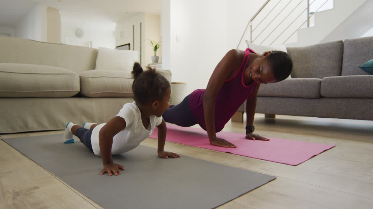 Happy african american mother and daughter doing yoga exercise at home