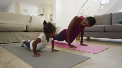 Happy-african-american-mother-and-daughter-doing-yoga-exercise-at-home