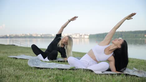 two young women do yoga in the morning on the shore of the lake bending their torsos two young women do yoga in the morning on the shore of the lake bending their torsos health concept care for emotional and physical health
