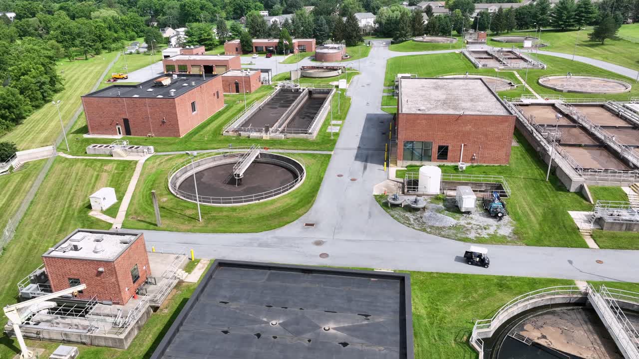 Golf caddy driving on area of sewage wastewater treatment facility in America. Aerial top downs sunny day in USA. Red brick buildings with circular tanks