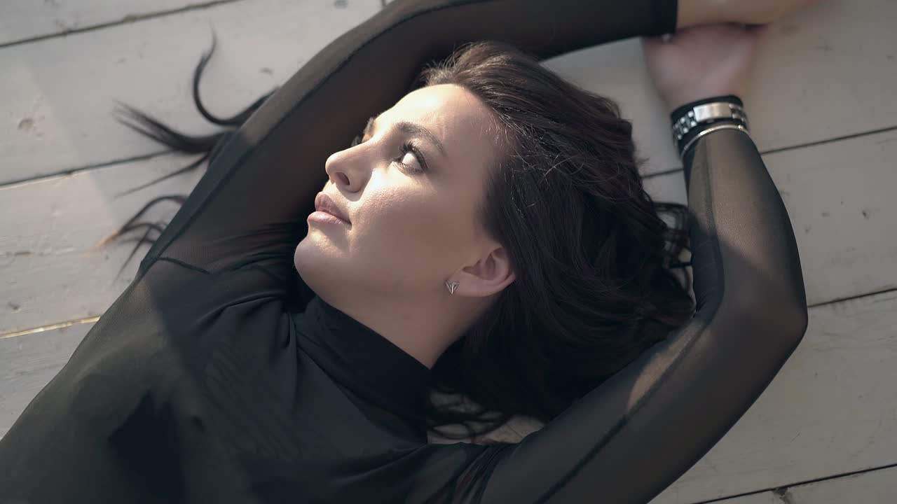 hermosa dama con maquillaje miente y arregla el cabello en el suelo de madera