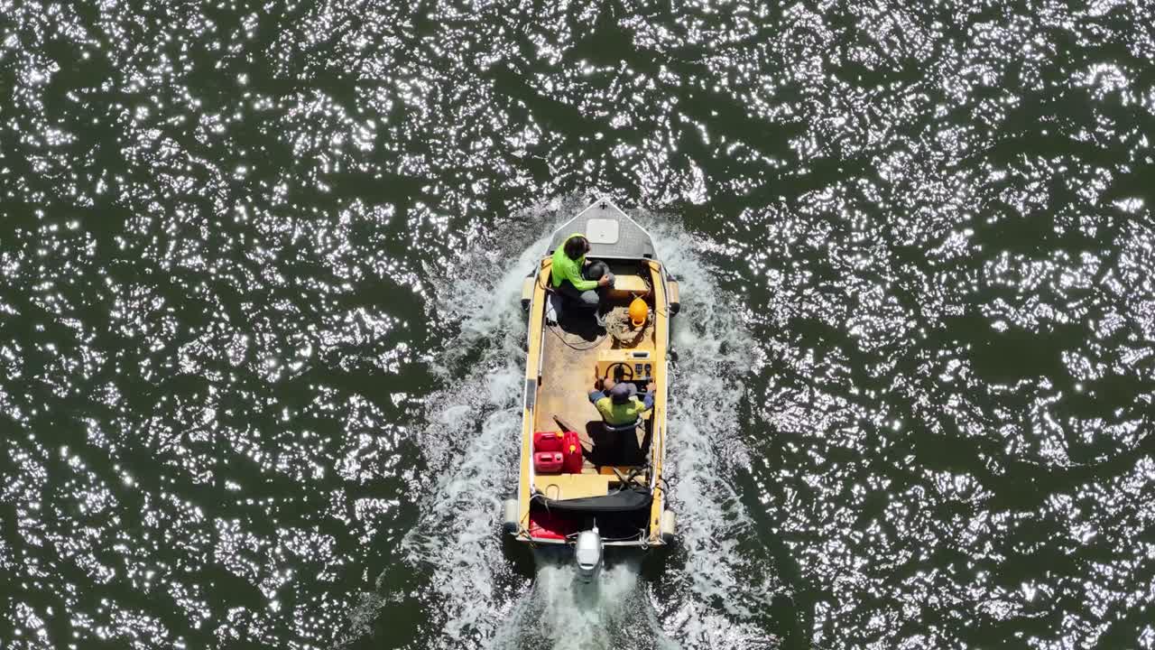 Tre lavoratori viaggiano in motoscafo su un corso d'acqua illuminato dal sole, ripresi dall'alto con un drone