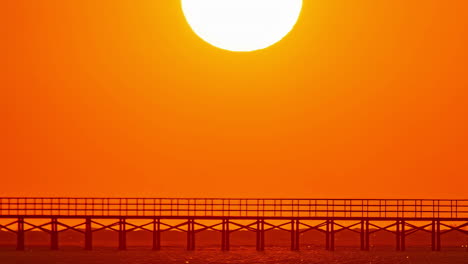 round glowing sun rises from behind seascape, time lapse view