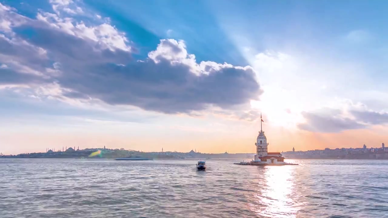 Leanderturm vor Sonnenuntergang mit farbenfrohen Wolken und Sonnenstrahlen Zeitraffer in Istanbul, Türkei, Kiz Kulesi Turm. Stadtsilhouette im Hintergrund mit Spiegelung auf dem Bosporus