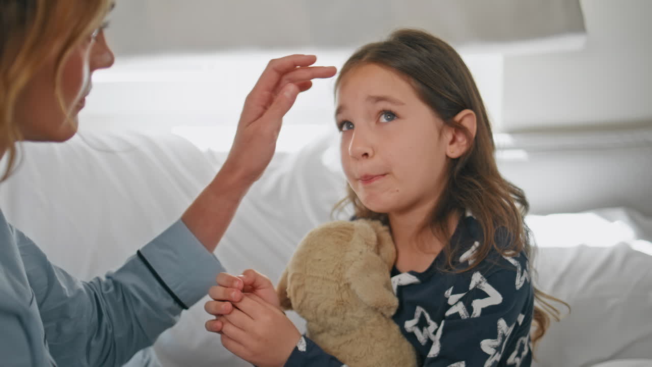 Unknown mother calming daughter touching hair at bed closeup. Toddler girl sad