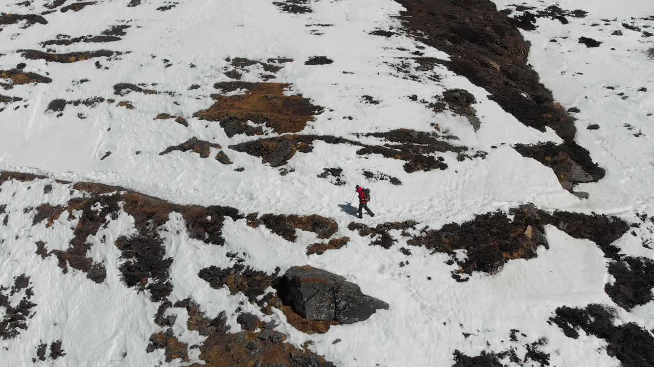 A solo trekker trekking through a snow trail in a sloppy hill. Sunny day afternoon in winter. Annapurna Conservation Area, Manang Valley, Nepal. Aerial Drone tracking shot from left side.