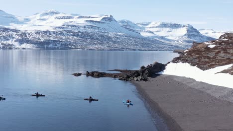 kayakers land on shore of remote holmanes peninsula in reydarfjordur fjord, aerial