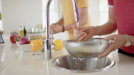 Diverse-couple-preparing-and-washing-fresh-vegetables-in-kitchen,-slow-motion