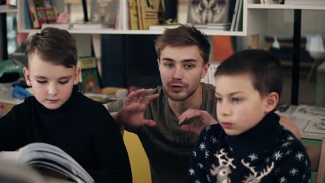 slow motion footage of young attractive male teacher explaining something to his two little pupils boys on a programming class. educational process.