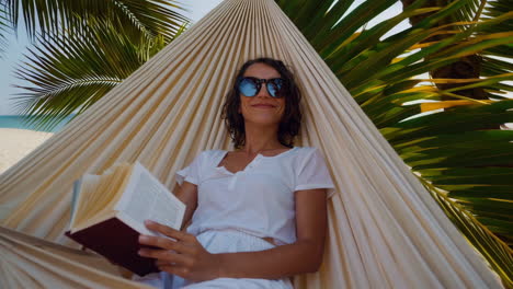 woman relaxing in a hammock on a tropical beach reading a book