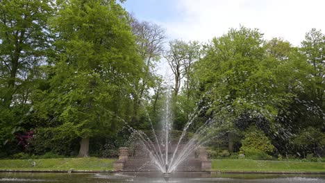 Ein-Laufender-Brunnen-In-Der-Mitte-Eines-Ruhigen-Teichs-Unter-Einem-Blauen-Bewölkten-Himmel-Während-Der-Frühen-Sprintzeit