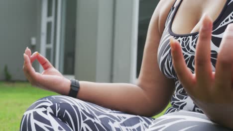 African-american-plus-size-woman-practicing-yoga,-sitting-meditating-in-garden