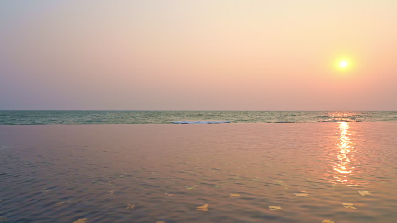 The bright pink and yellow sunset light reflects on the water of a resort infinity pool. Copy space