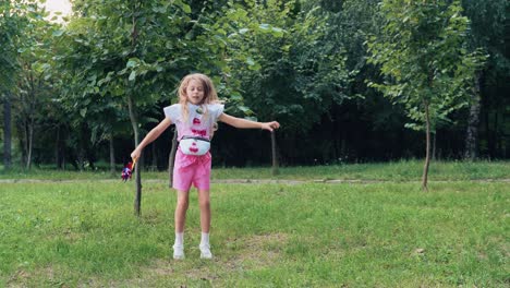 a little cheerful girl with a toy windmill in her hands in a park on the grass jumps, dances, plays. happy childhood