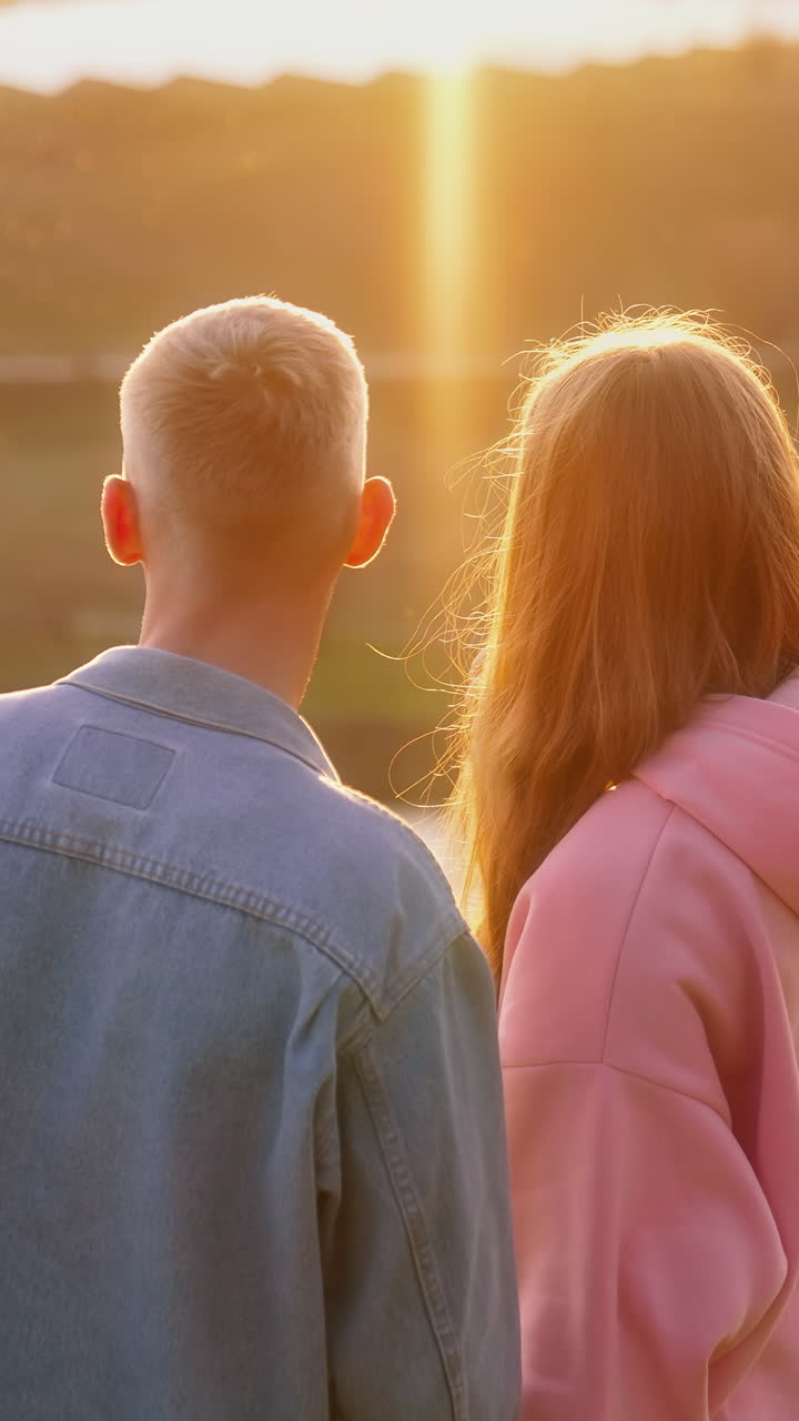 Couple in love in nature at sunset. Beautiful young girl and her boy friend admiring the setting sun over the river in autumn. Vertical video