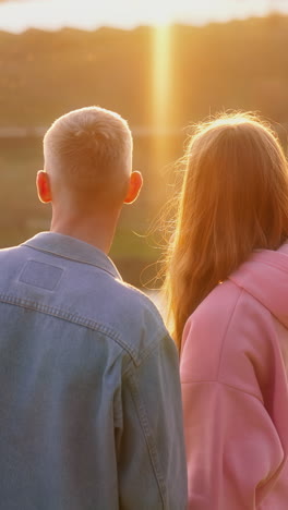 couple in love in nature at sunset. beautiful young girl and her boy friend admiring the setting sun over the river in autumn. vertical video